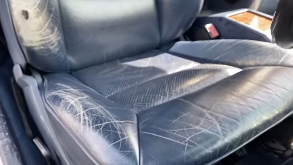 Close-up photograph of a leather car seat showing a developing crack and dry worn surface