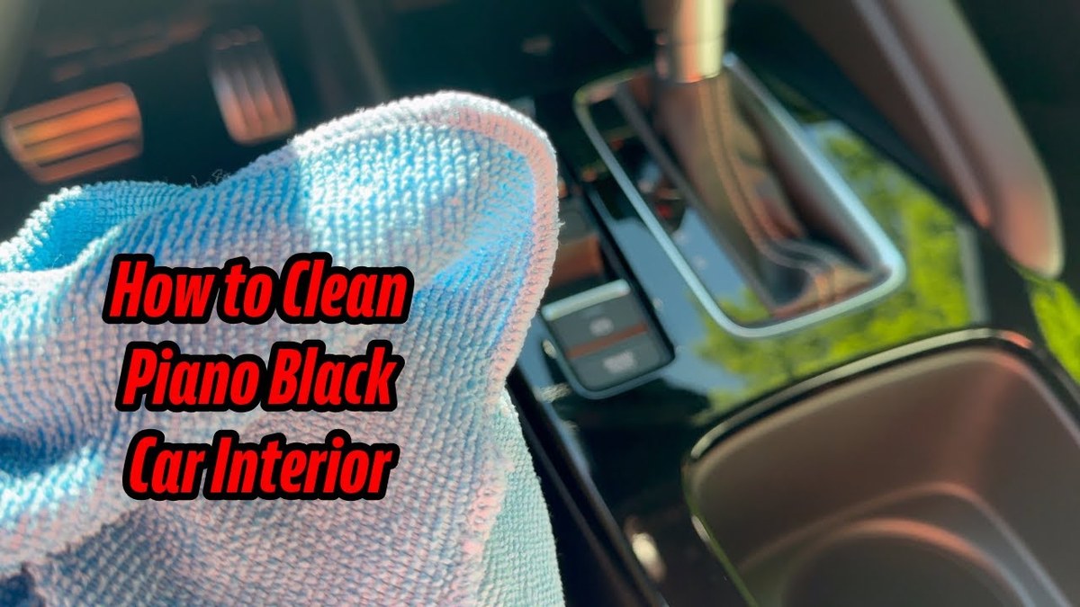 Hand wiping a glossy black car dashboard trim with a folded microfiber cloth