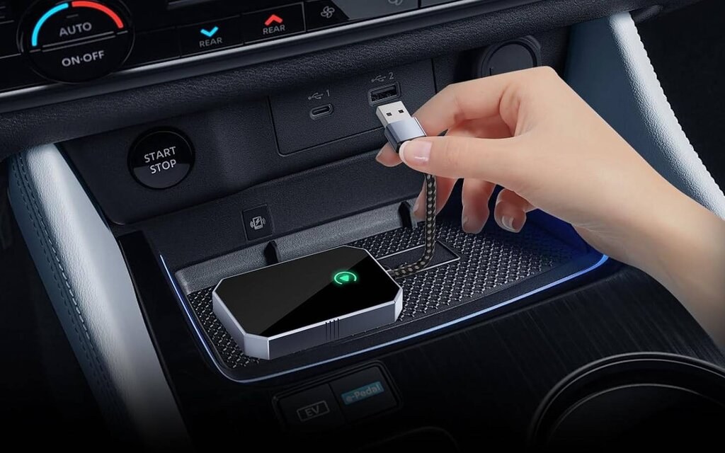 Hand pressing the reset button on a small wireless CarPlay adapter plugged into a car.
